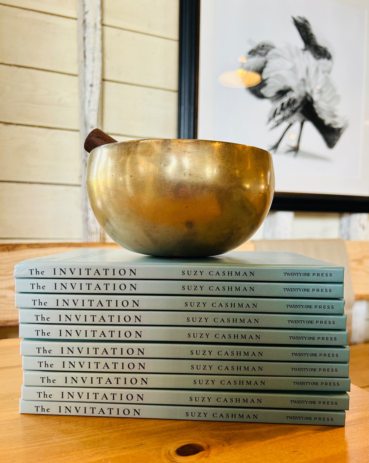 A stack of copies of The Invitation with a brass singing bowl